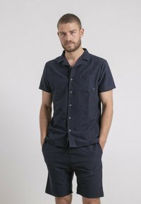 Chemise à manches courtes bleu marine avec boutons et short assorti, fabriqués dans un tissu léger avec une finition texturée, dotés d'une poche poitrine et d'un col rond.
