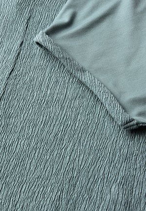 Zacht blauw stof met een gestructureerd, geribbeld oppervlak onder een gladde, gevouwen rand van een kledingstuk in dezelfde kleur.
