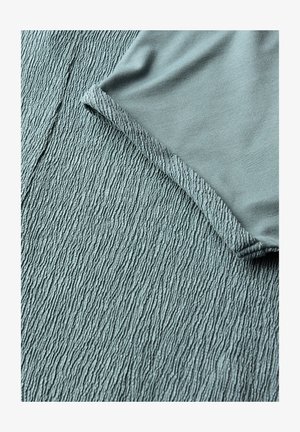 Weiches blaues Gewebe mit einer strukturierten, gerippten Oberfläche unter dem glatten, gefalteten Kleidungsrand in passender Farbe.