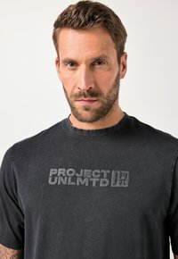 Černé bavlněné tričko s kulatým výstřihem, krátkými rukávy a texturovaným, vyraženým logem "PROJECT UNLMTD" na přední straně.