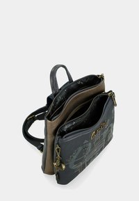 Sac à dos noir et marron avec plusieurs compartiments zippés, en cuir, surface texturée et détail de porte-clés décoratif.