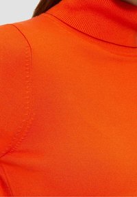 Světlý oranžový rolák vyrobený z hladkého, elastického materiálu. Obsahuje vysoký límec a žebrované detaily na krku a ramenou.