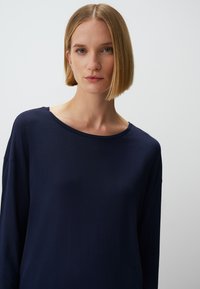 Marineblaues Langarmoberteil mit lockerer Passform, weitem Ausschnitt und weichem Material. Minimalistisches Design ohne sichtbare Muster oder Hardwaredetails.