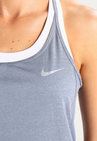 Světlomodré atletické tílko s texturovanou látkou, bílé vnitřní lemování, logo Nike a přiléhavý střih.