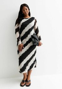 Robe à manches longues avec un motif tie-dye noir et crème, faite d'un tissu lisse. Associée à un sac à main noir et des sandales à brides.