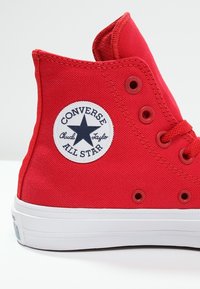 Baskets montantes rouges en toile avec semelle en caoutchouc blanche, dotées d'un écusson rond et d'œillets pour les lacets.