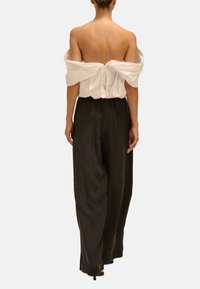 Biała bluzka typu off-the-shoulder z marszczonym tyłem, w zestawie z czarnymi, wysokogatunkowymi, szerokimi spodniami o gładkiej, zwiewnej tkaninie.