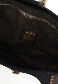 Interno di una borsa a tracolla nera in tessuto, con cerniera dorata e un patch quadrato in pelle con marchio e dettagli impressi.