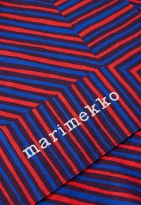 Βαμβακερό ύφασμα με έντονες κόκκινες και μπλε διαγώνιες ρίγες σε σκοτεινό φόντο, με προσκολλημένη λευκή ετικέτα "marimekko".