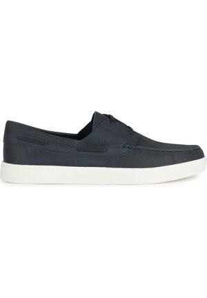 Chaussures en toile bleu marine à enfiler avec une finition texturée, semelle en caoutchouc blanc et couture décorative le long des bords. Présente un laçage minimal.