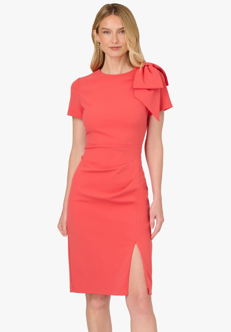 Koralowa dopasowana sukienka z krótkimi rękawami, kokardą na jednym ramieniu i rozcięciem z boku. Wykonana z gładkiej tkaniny o strukturalnym kroju.