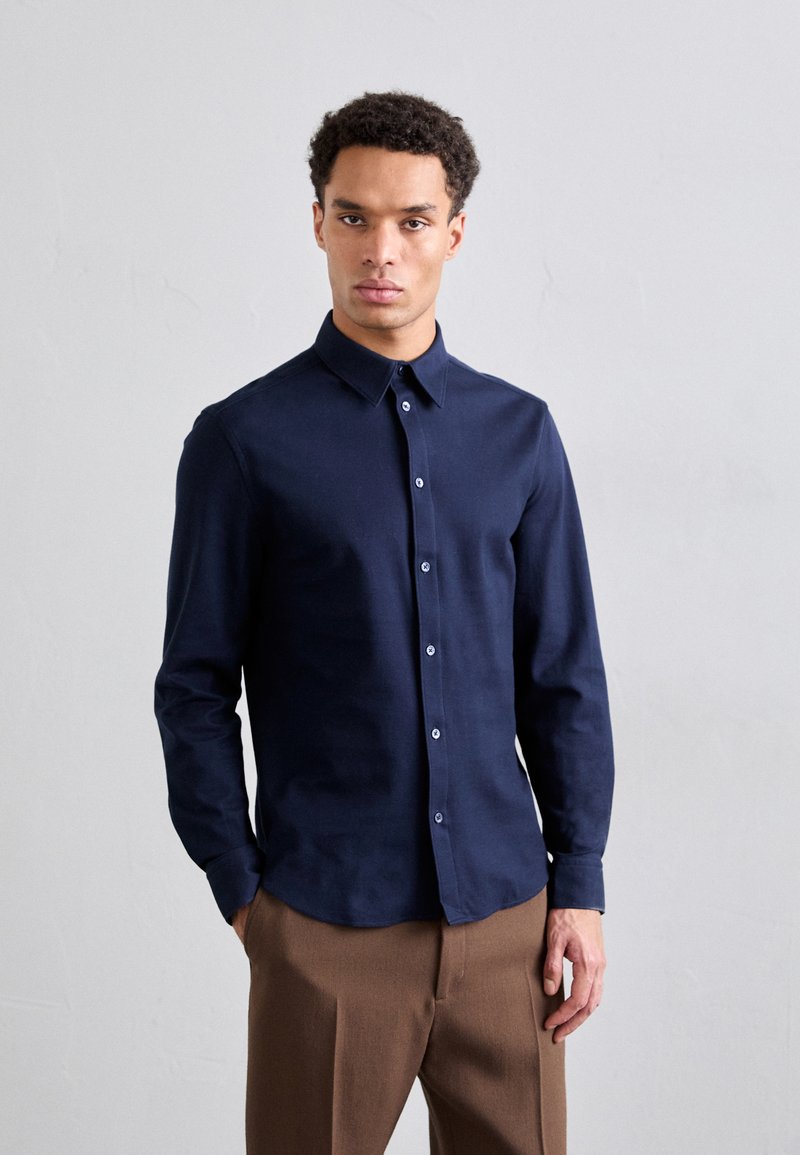 Camisa de manga larga azul marino de tejido suave, con cuello clásico, cierre de botones en el frente y mangas abotonadas.