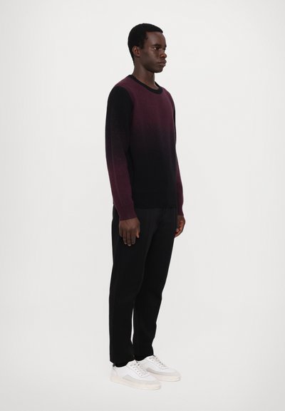 Pulover cu gradient de la burgund până la negru, guler rotund, mâneci lungi, purtat cu pantaloni negri și adidași albi pe un model, într-un fundal simplu.
