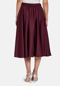 Kirsche Satinrock mit einem elastischen Bund, in einer fließenden A-Linie, die bis zur Wade reicht. Getragen mit silbernen High-Heels.