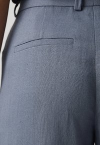 Pantaloni tessuti di un blu chiaro, con una sottile trama, dotati di una tasca posteriore e un taglio sartoriale, mostrati da un angolo laterale.