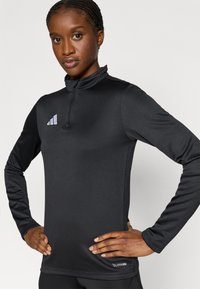 Μαύρο αθλητικό τοπ με μακρύ μανίκι, ψεύτικο γιακά και φερμουάρ στη λαιμόκοψη. Διαθέτει ραφές χωρίς όγκο και τη λευκή επιγραφή "CLIMACOOL" στο κάτω μέρος.