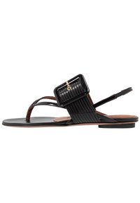 Sandalo in pelle nera con suola piatta, dotato di una larga fascia con finitura texture e un accento decorativo a forma di fibbia.