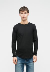 Μαύρο μπλουζάκι με μακριά μανίκια και στρογγυλή τον neckline, λεία υφή, εφαρμοστή γραμμή και ελαφρώς καμπυλωτό γύρισμα, συνδυασμένο με μπλε τζιν.