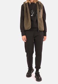 Suéter negro con un diseño gráfico, chaleco de forro polar verde oliva, pantalones jogger negros y zapatillas negras. Texturas suaves, ajuste informal y capas.