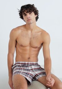 Boxers de cuadros para hombre hechos de una tela suave, con una mezcla de colores marrón, gris y blanco, con una cinturilla elástica y un corte holgado.
