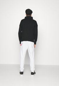 Zwarte geribde trui met hoge kraag, gecombineerd met witte sweatpants met een rode accenten en zwarte sneakers. Eenvoudige, casual look.
