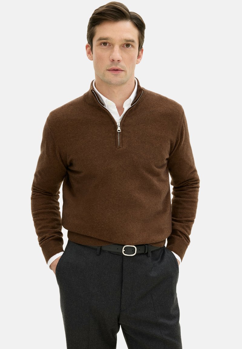 Brauner Reißverschluss-Pullover mit gestrickter Textur, Stehkragen und weißem Hemd darunter. Kombiniert mit dunklen Hosen und einem schwarzen Gürtel.