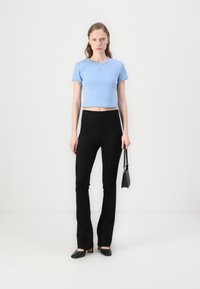 Light blue cropped t-shirt with short sleeves, paired with high-waisted black flared pants and black heeled shoes, holding a small black bag.