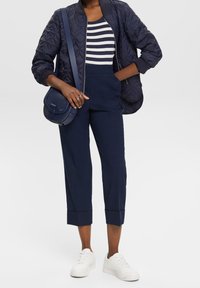 Marinblå quiltad bomberjacka, randig marinblå och vit topp, skräddarsydda marinblå cropped byxor, vita sneakers och en marinblå crossbody-väska.