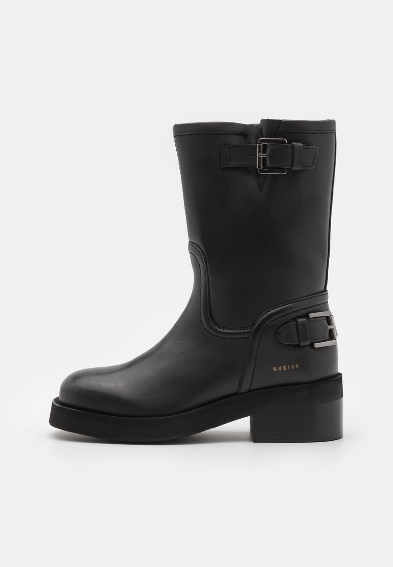 Bottillon en cuir noir avec un bout arrondi, un talon bloc, un détail de boucle sur le côté et une finition texturée. Présente un branding subtil en doré.