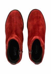 Bottines en daim rouge avec une texture lisse, dotées d'une fermeture éclair sur le côté et d'un design à bout rond. Étiquette de marque visible à l'intérieur.