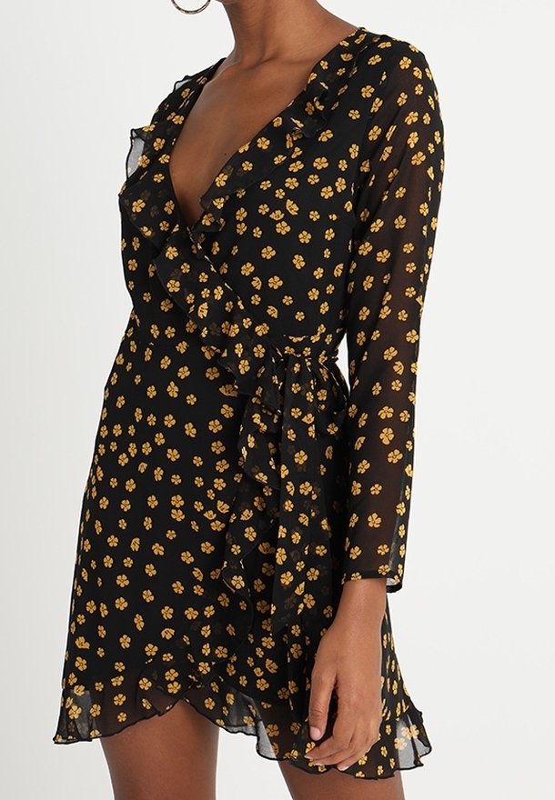 Robe portefeuille noire à motif floral jaune, col et ourlet à volants, manches longues transparentes et lien latéral à la taille.