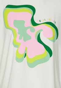 Vit t-shirt med lager av abstrakta former i rosa, grönt och gult, med texten "HEJ FRAMTID" i ett lekfullt teckensnitt.