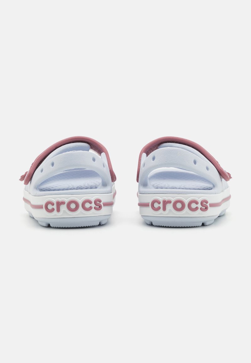 Crocs Sandalen; Rückansicht, die einen weißen Körper mit einem pinken Riemen zeigt. Text "crocs" in Pink auf der Ferse; glatte Gummibeschaffenheit.