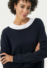Maglione navy con colletto a girocollo bianco. Materiale in maglia morbido, vestibilità ampia e maniche lunghe. Orlo curvo e polsini a costine per dettagli.