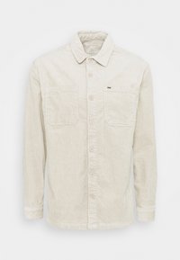 Camisa de pana beige de manga larga con botones en la parte delantera, dos bolsillos en el pecho y cuello, mostrada sobre un fondo blanco.