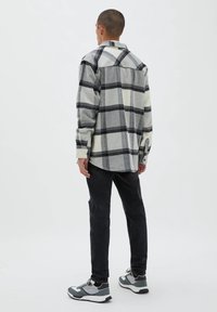 Gray and white plaid flannel shirt with a rounded hem, button cuffs, and a back yoke, worn with black jeans and gray sneakers.