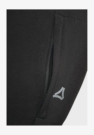 Schwarze Sportleggings mit einem Reißverschlusstasche und einem reflektierenden Logodetail an der unteren Seite. Weiche, glatte Textur.