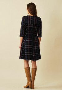 En marinblårutig klänning med trekvartsärmar, utsvängd kjol och dragkedjedetalj, kombinerad med höga, beige klackstövlar.