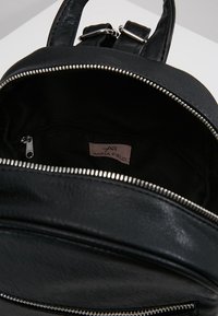 Czarny skórzany plecak z srebrnymi okuciami. Główna komora na suwak odsłania czarne wnętrze oraz małą wewnętrzną kieszeń na suwak. Widoczna etykieta marki.