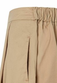Jupe en tissu beige avec une taille élastique, dotée de plis et d'une texture lisse. L'ourlet est droit, sans accents ni motifs visibles.
