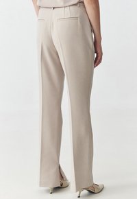 Pantaloni beige con taglio dritto, dotati di tasche posteriori e spacchi laterali all'orlo, realizzati in un tessuto morbido.