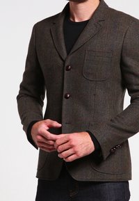Brun herringbone-blazer med en enda bröstficka, två knappar och tygtextur. Har mörka knappar och skräddarsydd passform.