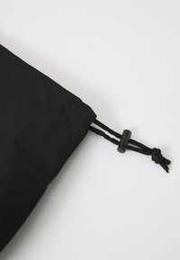 Drawstring bag made of black fabric, featuring a cinched top with two black cords and a small toggle for closure. Smooth texture, minimal design.