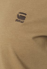 Brun bomullstyg med ribbad textur som har en mörk logotyp i det övre vänstra hörnet som lyder "RAW."