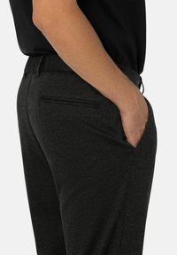 Graue Freizeitpants mit elastischem Bund, seitlichem Taschen und glattem Material, seitlich dargestellt. Keine auffälligen Muster oder Akzente.