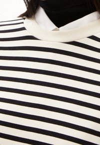 Proužkovaný bavlněný top s vodorovnými námořnicky modrými a krémovými pruhy, žebrovaným výstřihem a vrstveným límečkem s černým rolákem pod ním.