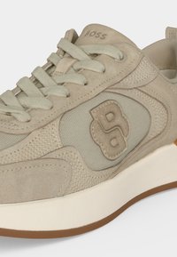 Baskets beiges en daim et mesh avec fermeture à lacets, logo "B" en relief sur le côté, "BOSS" embossé sur la languette, et semelle blanche avec semelle extérieure marron.
