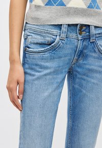 Svetlomodré džínsové nohavice s mierne vyblednutou textúrou, s piatimi vreckami a zapínaním na gombíky. Tkanina vykazuje klasický tkaný vzor.