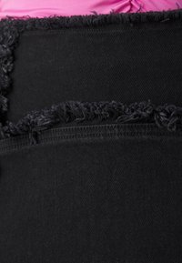 Gros plan sur un tissu en denim noir aux bords effilochés sur deux morceaux qui se chevauchent, sur un fond rose.