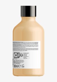 Kapsel-formad flaska i matt pastellpersika med ett svart lock. Har en vit etikett med produktinformation, ingredienser och återvinningssymboler. 300 ml.